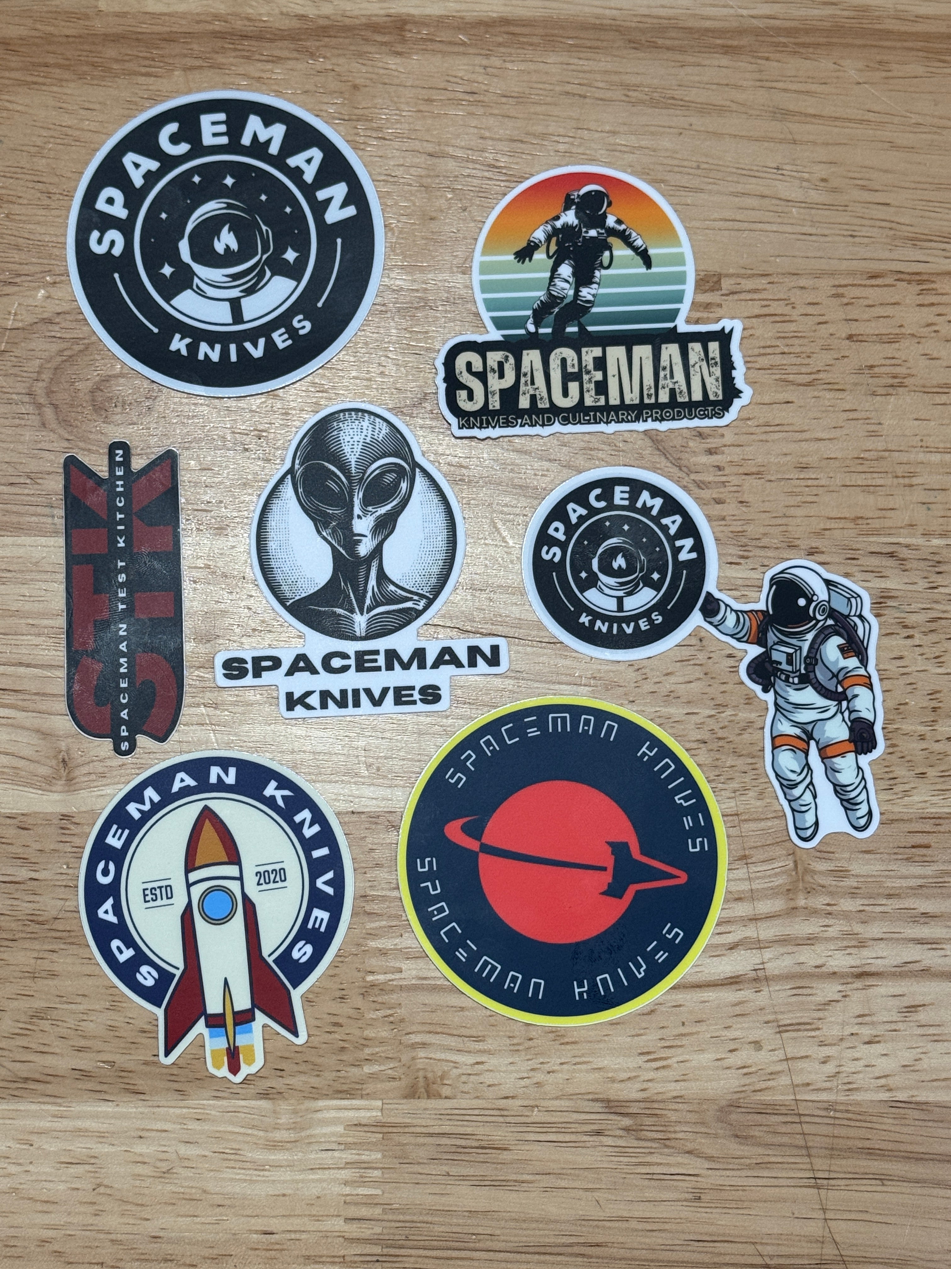 Collection of Spaceman Knives brand stickers on a wooden surface