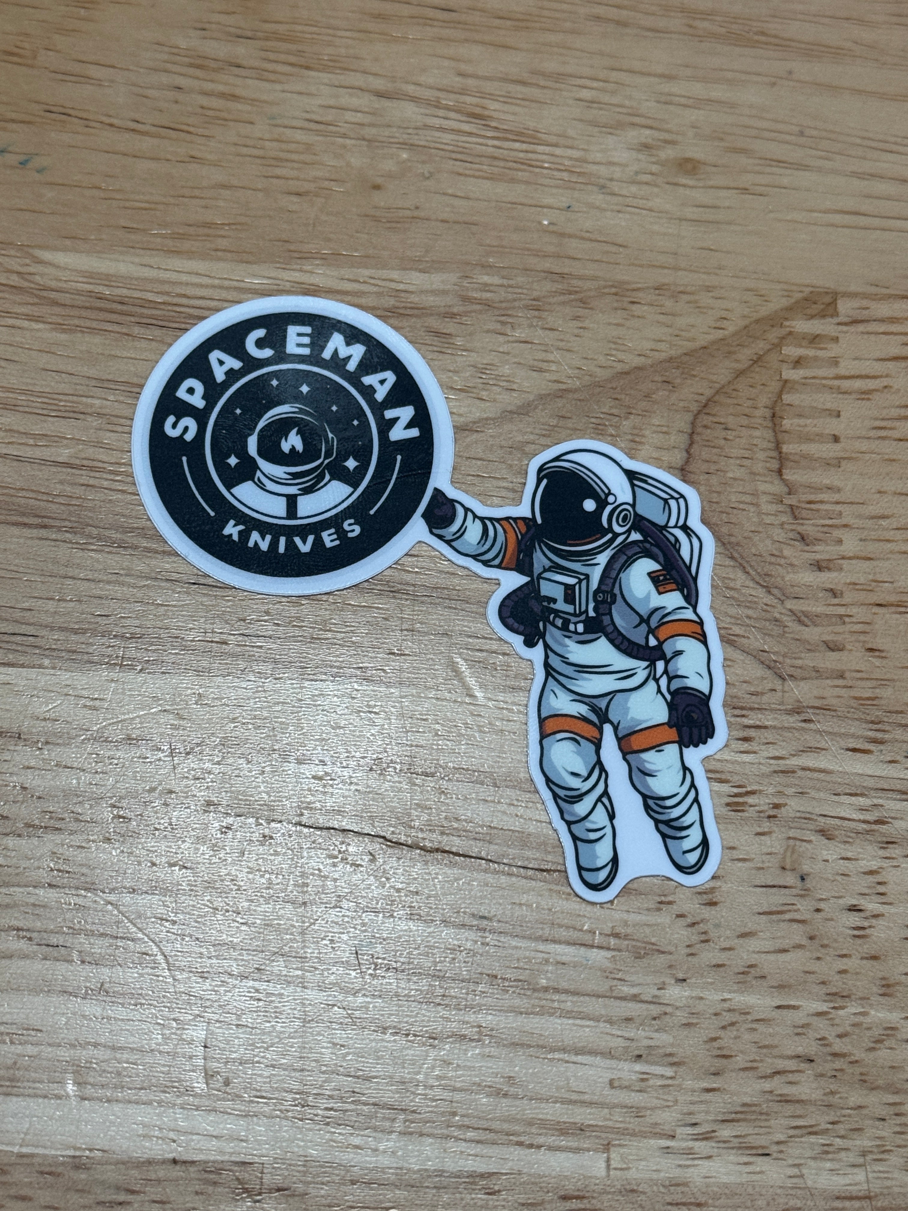 Sticker of an astronaut and 'Spaceman Stickers' logo on a wooden surface