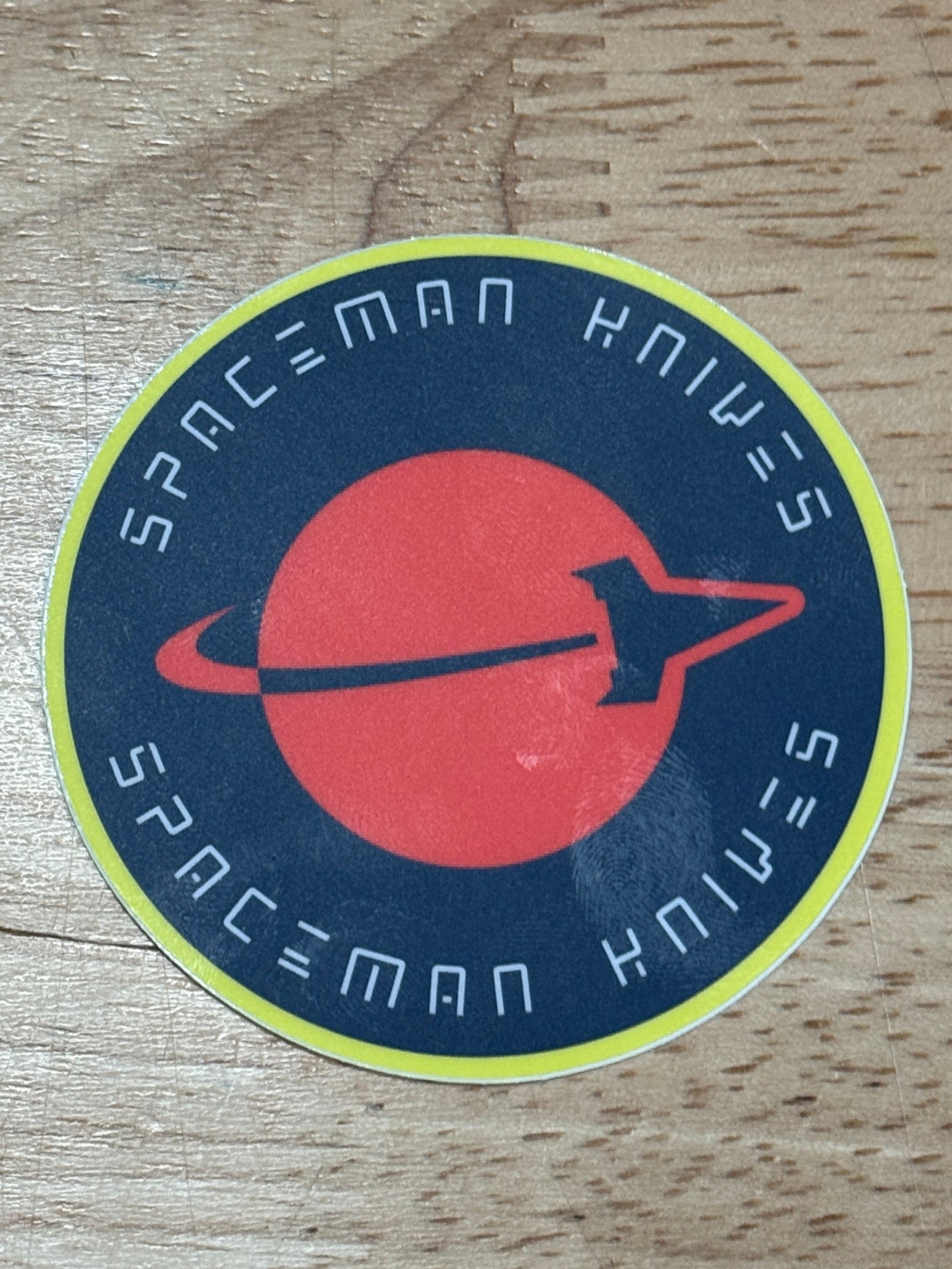 Round sticker with a red symbol and blue text on a wooden surface